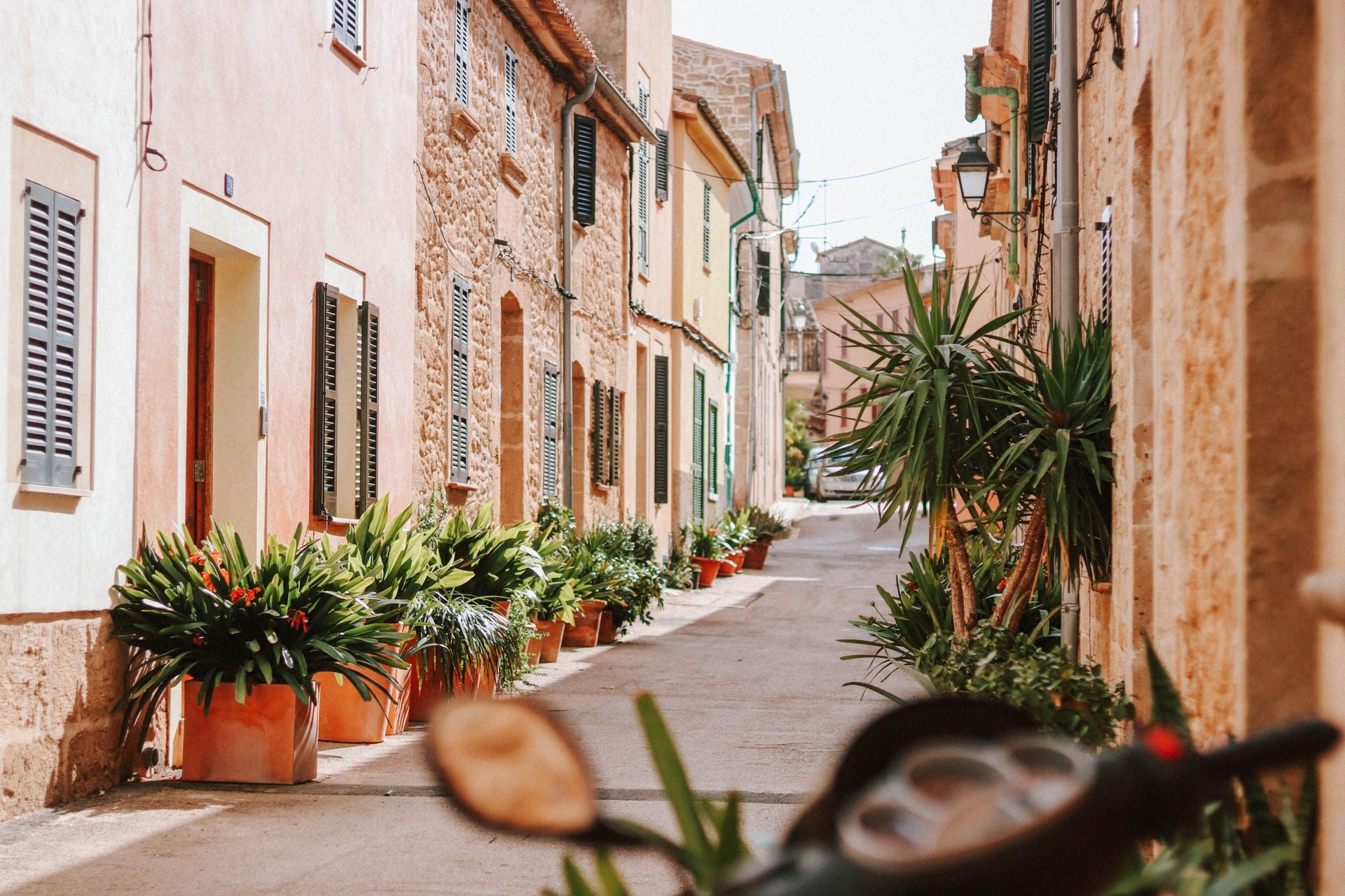 Sunlit Mediterranean street in Mallorca with stone buildings and potted plants